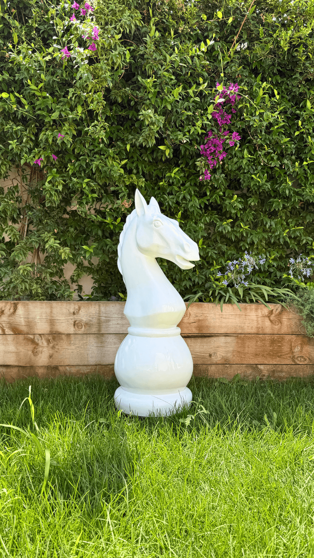 Statue Échecs - GRANDIOSE représentant un cavalier blanc en résine de 1m40, posée sur pelouse devant haie fleurie. Design contemporain pour jardin.