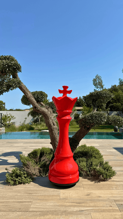 Statue d’échecs géante rouge en résine représentant une reine, modèle GRANDIOSE, posée sur une terrasse extérieure près d’un arbre taillé. Idéale pour décoration de jardin ou espace public.