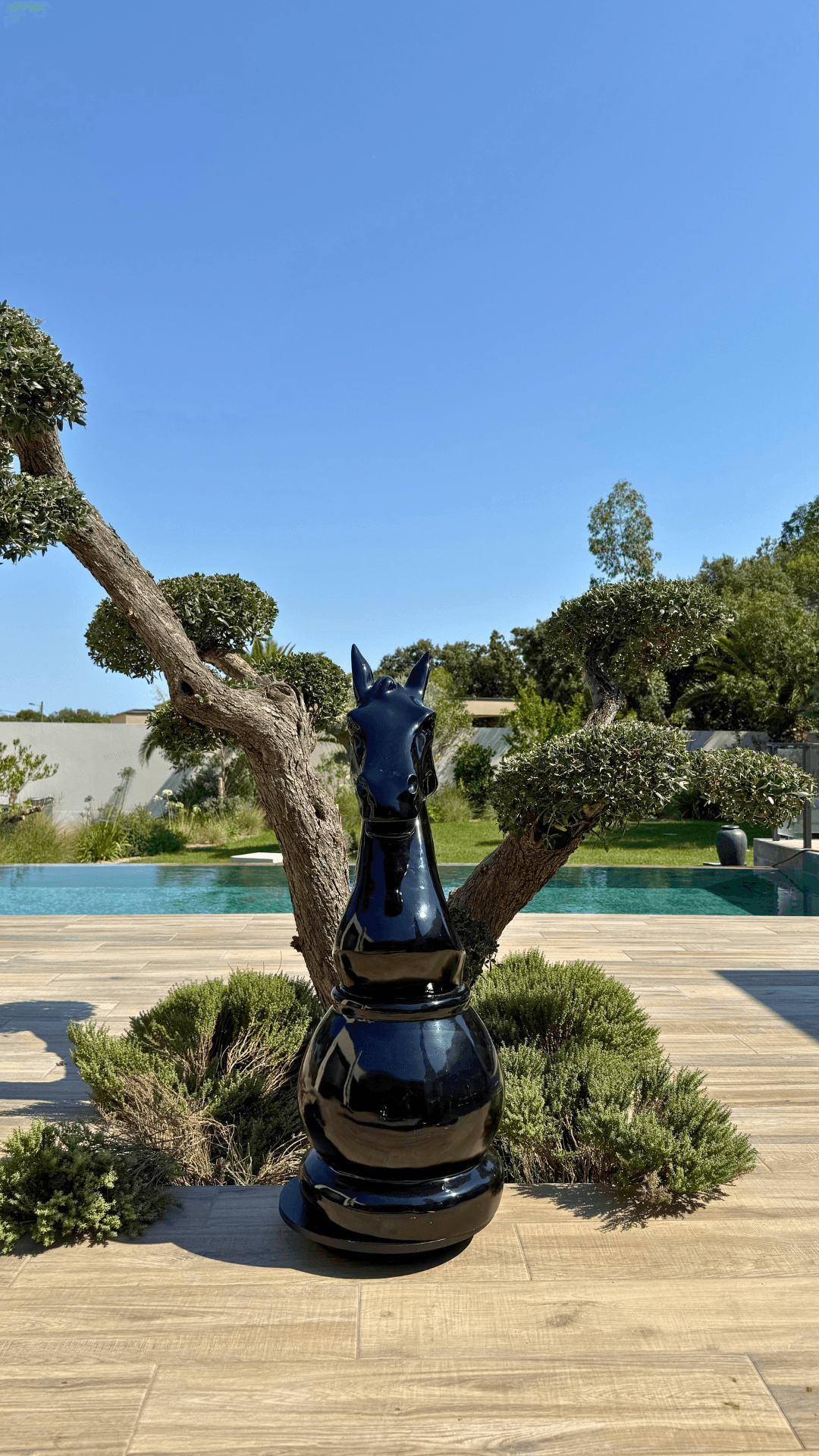 Statue d’échecs géante en résine noire représentant un cavalier, modèle GRANDIOSE, placée sur une terrasse en bois près d’un jardin paysager moderne.