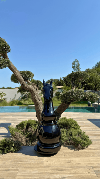 Statue d’échecs géante en résine noire représentant un cavalier, modèle GRANDIOSE, placée sur une terrasse en bois près d’un jardin paysager moderne.