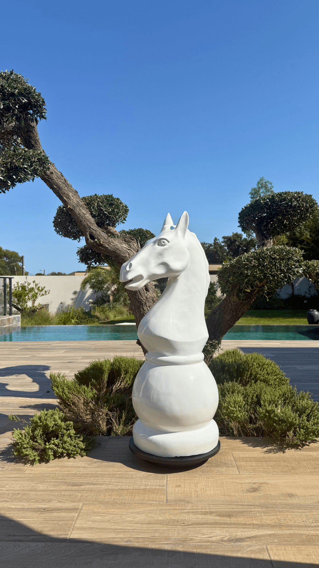 Statue Échecs - GRANDIOSE en forme de cavalier blanc de 1m40 en résine, posée sur une terrasse extérieure près d’un jardin paysager moderne.